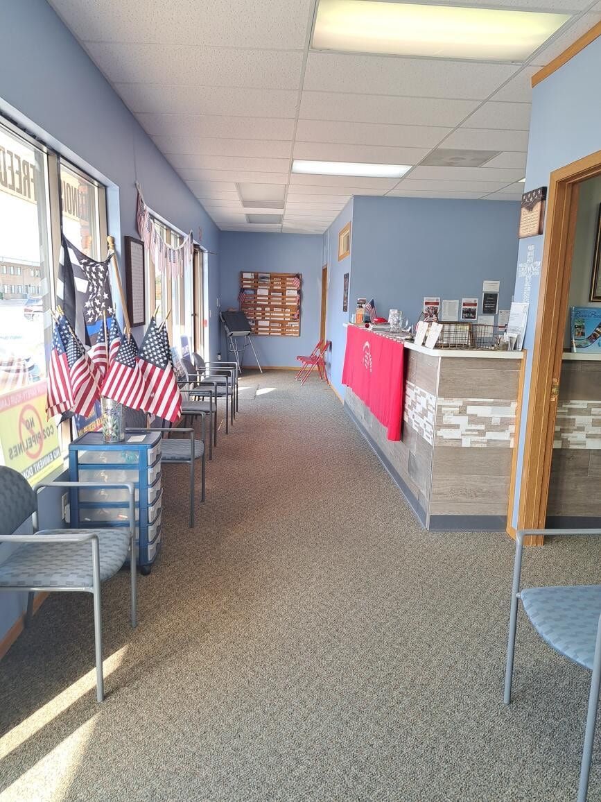 Empty waiting area with blue chairs, American flags, and a reception counter with a red cloth.