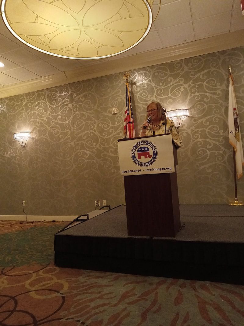 Person speaking at a podium on a stage in a banquet hall