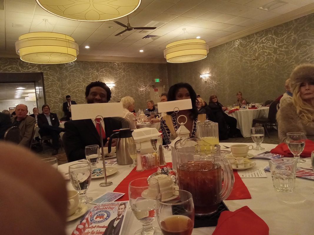 Banquet table with drinks and red napkins; two people hold menus under warm ceiling lights.