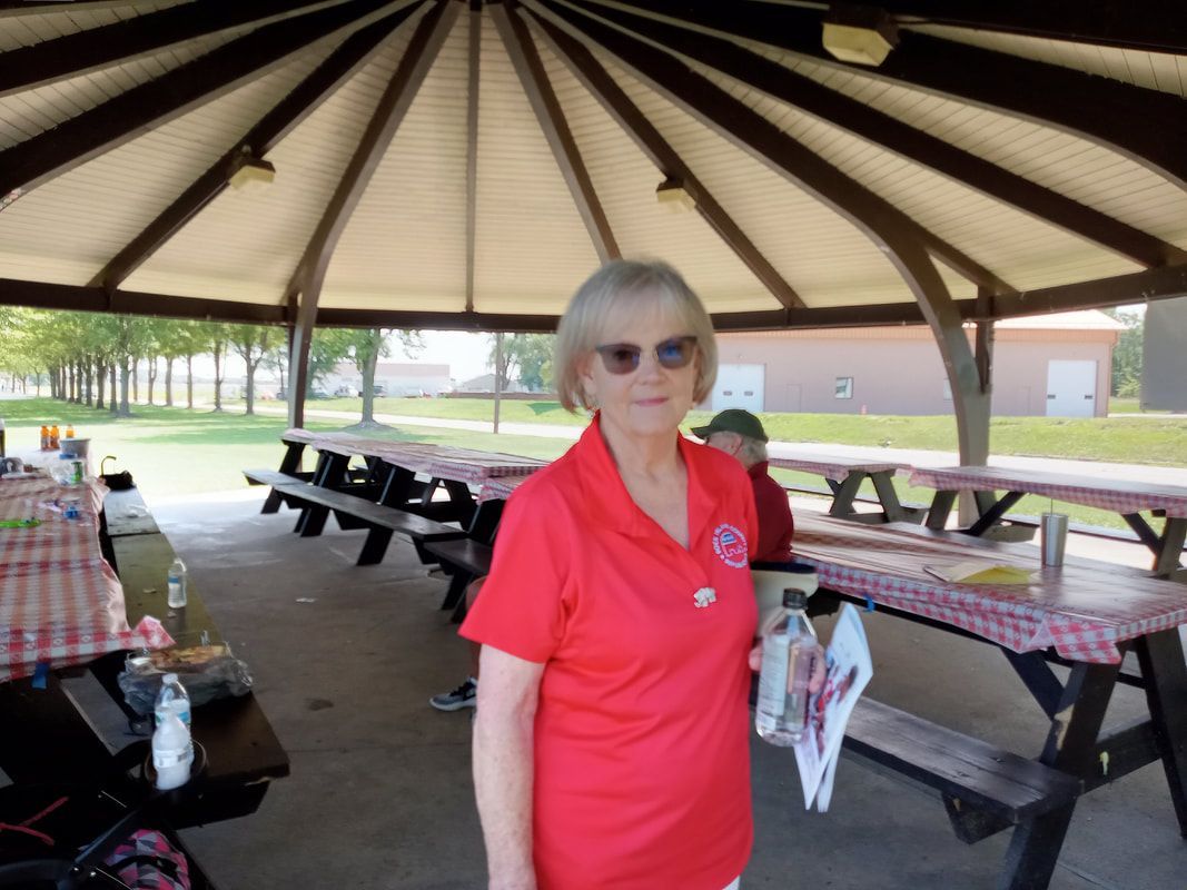 Woman in red shirt standing in a picnic pavilion with tables and benches