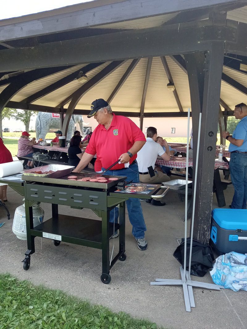 Man in a red shirt cooking at a grill under a gazebo at an outdoor gathering
