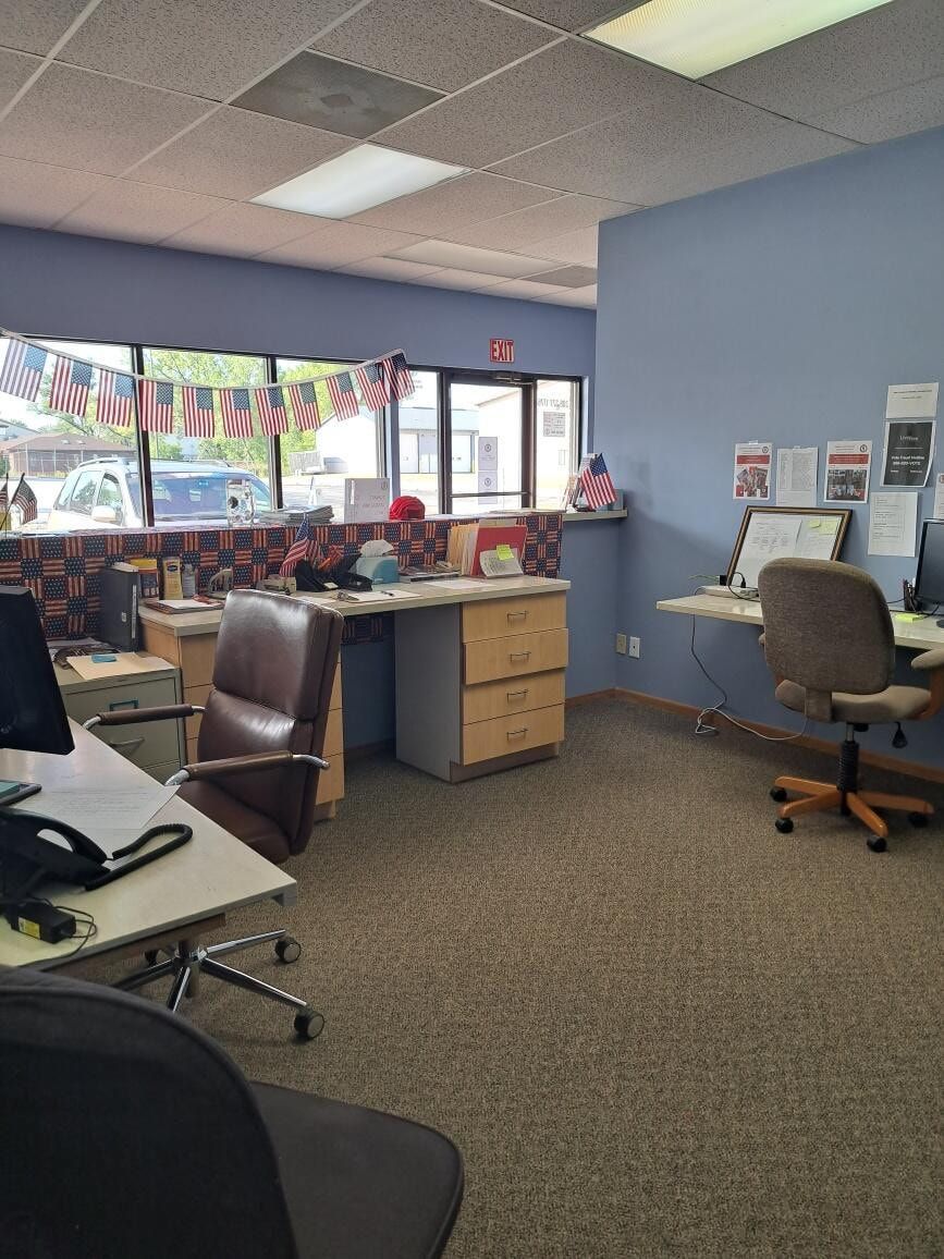 Office cubicles with desks, chairs, and computers beside a window decorated with colorful bunting.