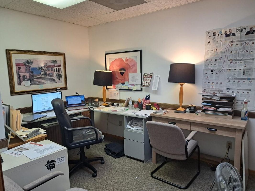 Office with two desks, computer monitors, chairs, lamps, and framed artwork on the walls.