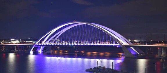 Purple-lit arch bridge glowing over calm water at night