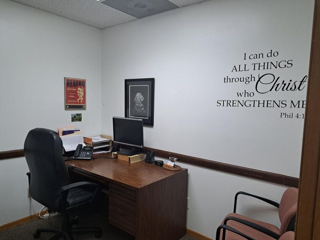 Office with desk, computer monitors, black chairs, and wall decal reading about strength in Christ