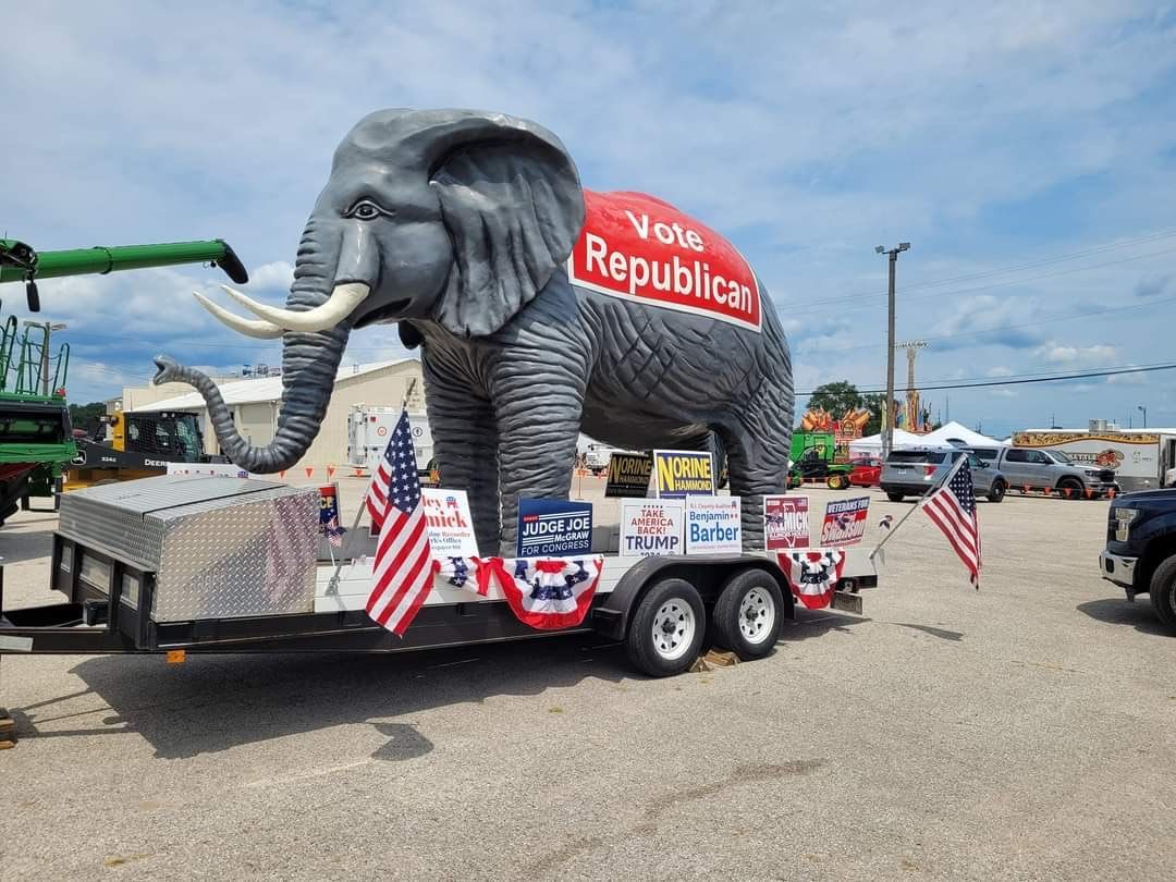 Giant elephant float with “Republican” sign, red-white-blue bunting, and U.S. flags on a trailer in a parking lot