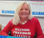 Woman in a red Illinois Freedom Alliance shirt smiling in front of an Illinois Alliance sign