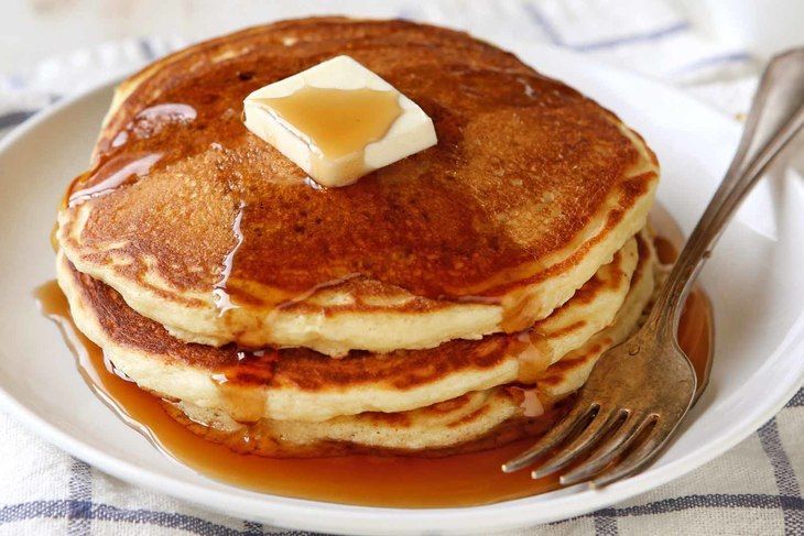 Stack of pancakes with syrup and a pat of butter on a plate, with a fork beside it