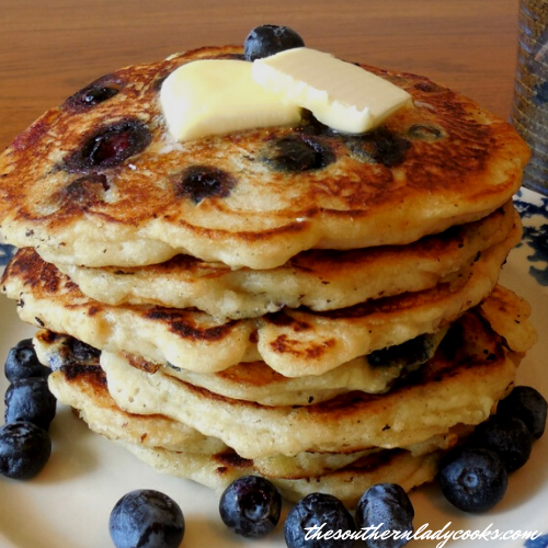 Stack of blueberry pancakes topped with butter, with fresh blueberries on a wooden table