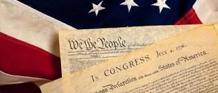 U.S. Constitution on a table with the American flag in the background