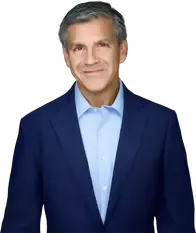 Portrait of a man in a navy suit and light blue shirt, standing against a white background.