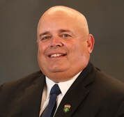 Smiling bald man in a dark suit and blue tie against a plain background