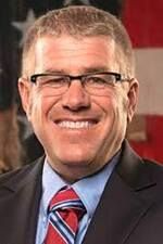 Smiling man in glasses and suit with red striped tie against a blurred background