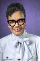 Portrait of a smiling person in glasses, wearing a light blouse with a bow, against a purple background