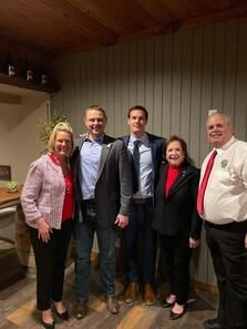 Five people posing together indoors, wearing semi-formal clothes in a wood-paneled room.
