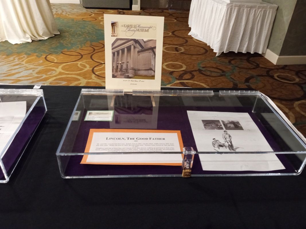 Display case with an old book and framed documents on a patterned carpeted floor