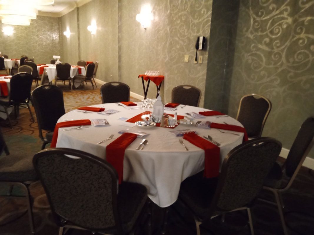 Round banquet table set with red napkins and glassware in a dimly lit dining hall.