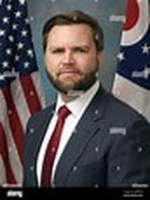 Man in navy suit and red tie standing before U.S. and Ohio flags