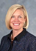 Smiling blonde woman in a black blazer against a gray studio background