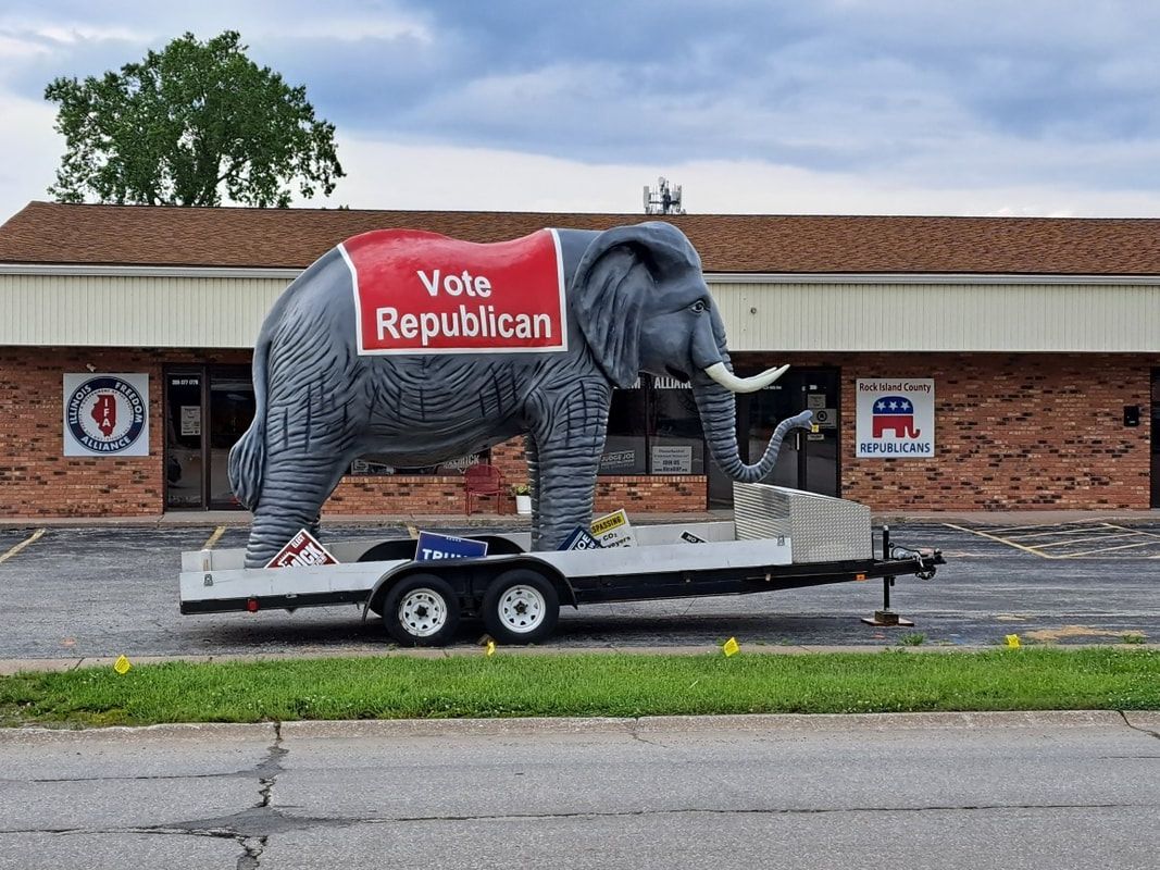 Gray elephant lawn sculpture on trailer with a red “Vote Republican” blanket in front of a brick building