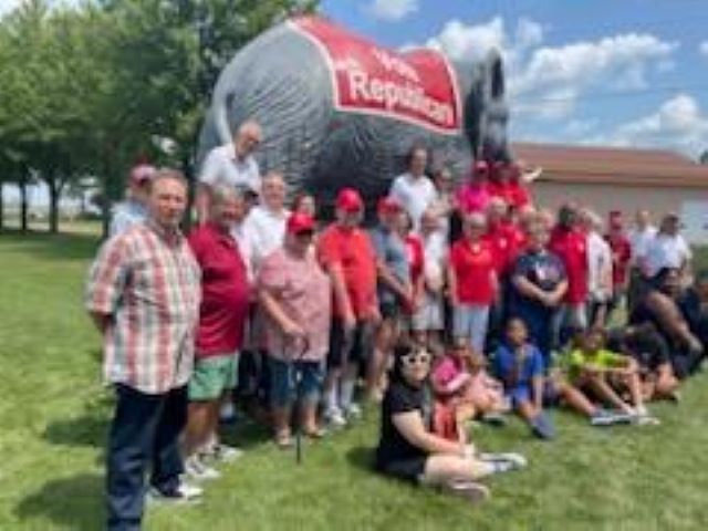 Group of people posing outdoors beside a giant red-and-silver Reynolds trailer in front of a building