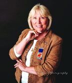 Portrait of a smiling woman in a tan jacket against a black background