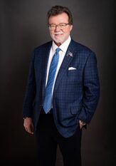 Studio portrait of a smiling man in a blue suit, white shirt, and blue tie on a dark background