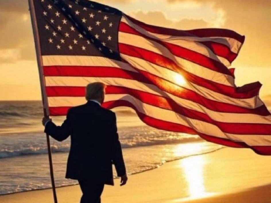 Person holding a U.S. flag on a beach at sunset, with golden light over the water.