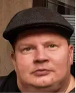 Close-up of a man wearing a dark flat cap, looking at the camera with a neutral expression