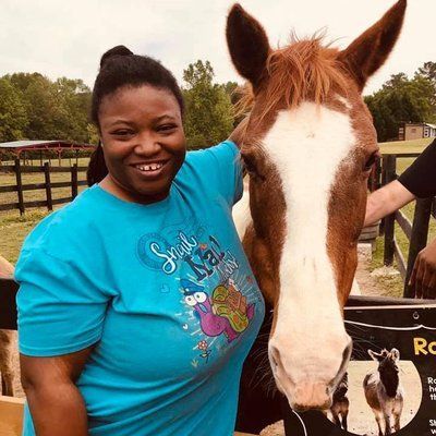 A woman in a blue shirt is standing next to a brown and white horse.