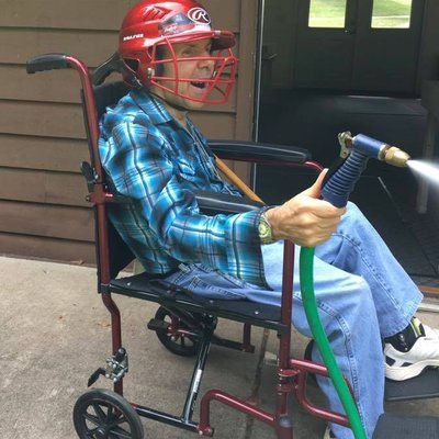 A man in a wheelchair is wearing a baseball helmet and holding a hose