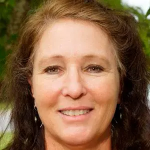 A close up of a woman 's face smiling in front of a tree.