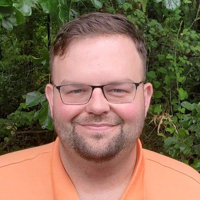 A man wearing glasses and an orange shirt is smiling for the camera.