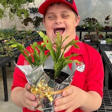 A man in a red shirt is holding a potted plant in his hands.