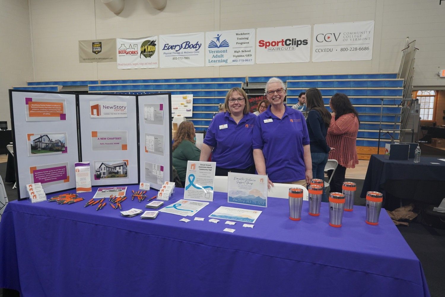 Two women are standing at a table with a purple table cloth.