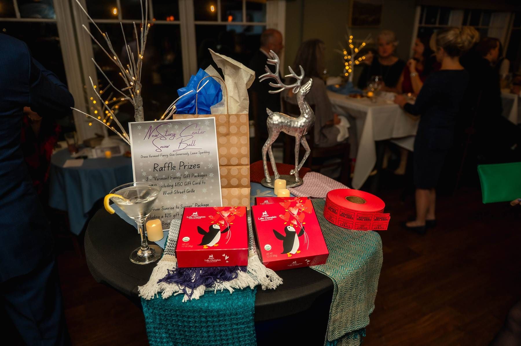 A table with decorations and gifts at an event, including a silver reindeer and two red penguin-themed boxes.