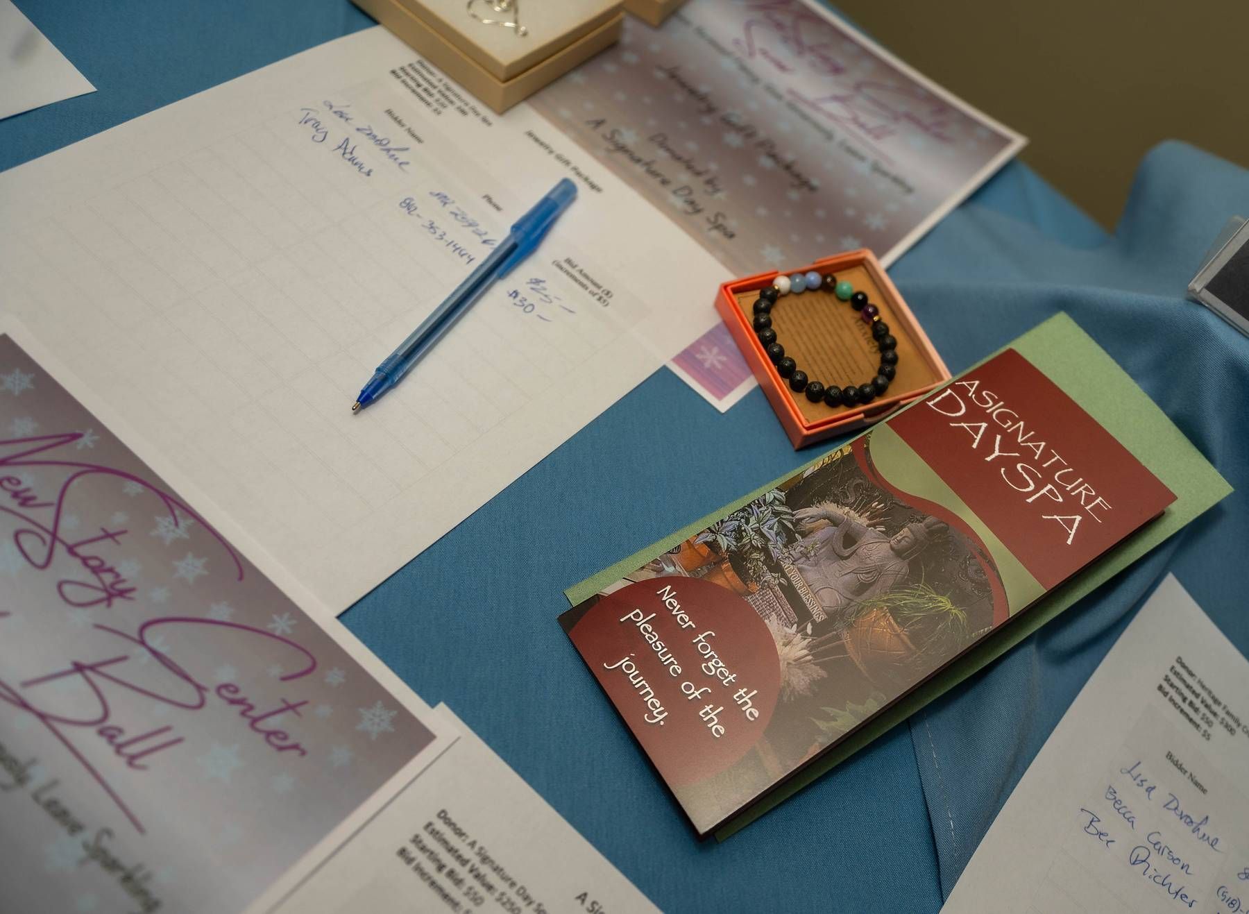 Table with papers, pen, jewelry, and brochure, possibly for an event or giveaway.
