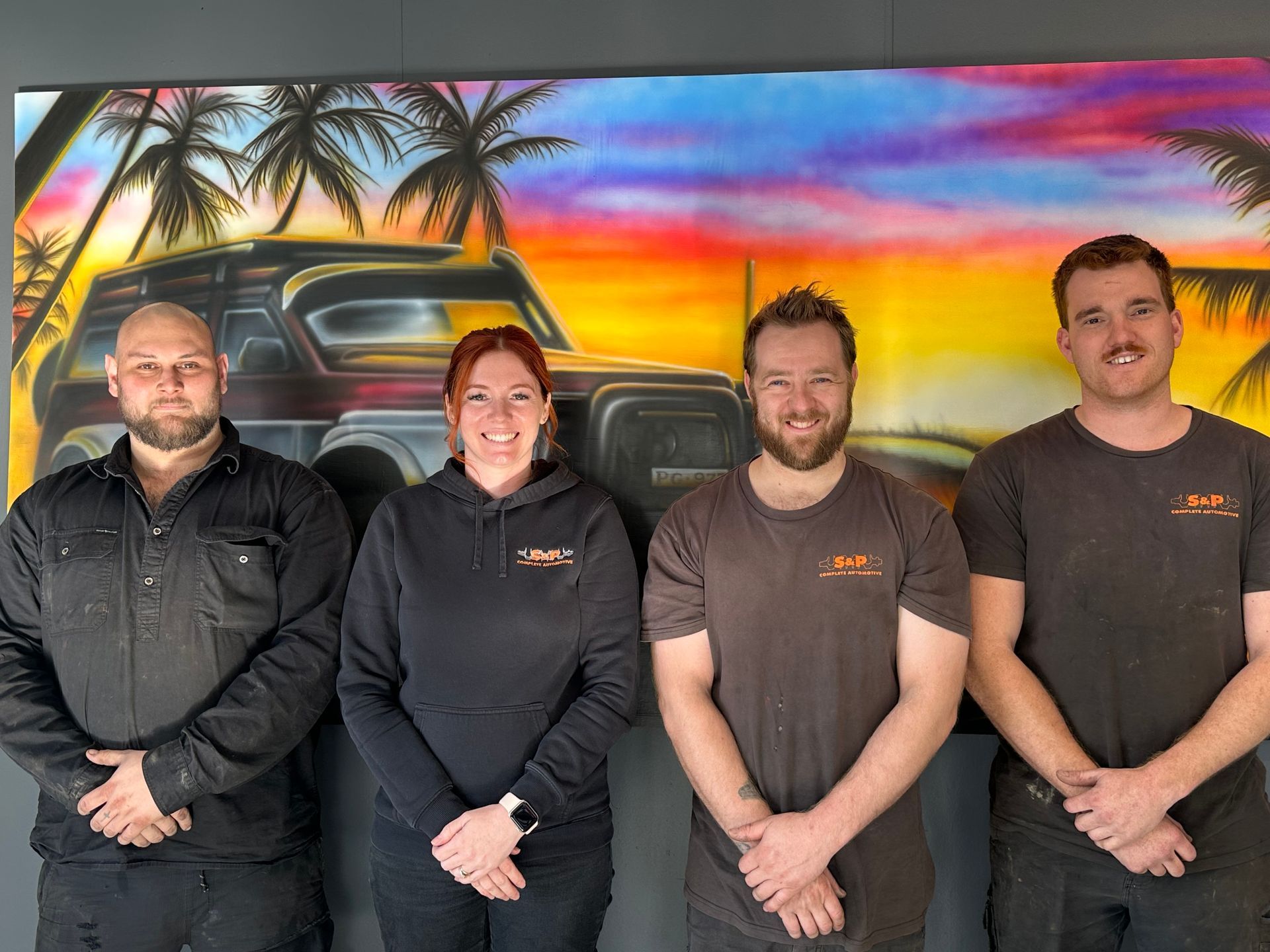 Four People Posing in Front of A Mural of A Vehicle and Sunset — S&P Complete Automotive in Port Macquarie, NSW