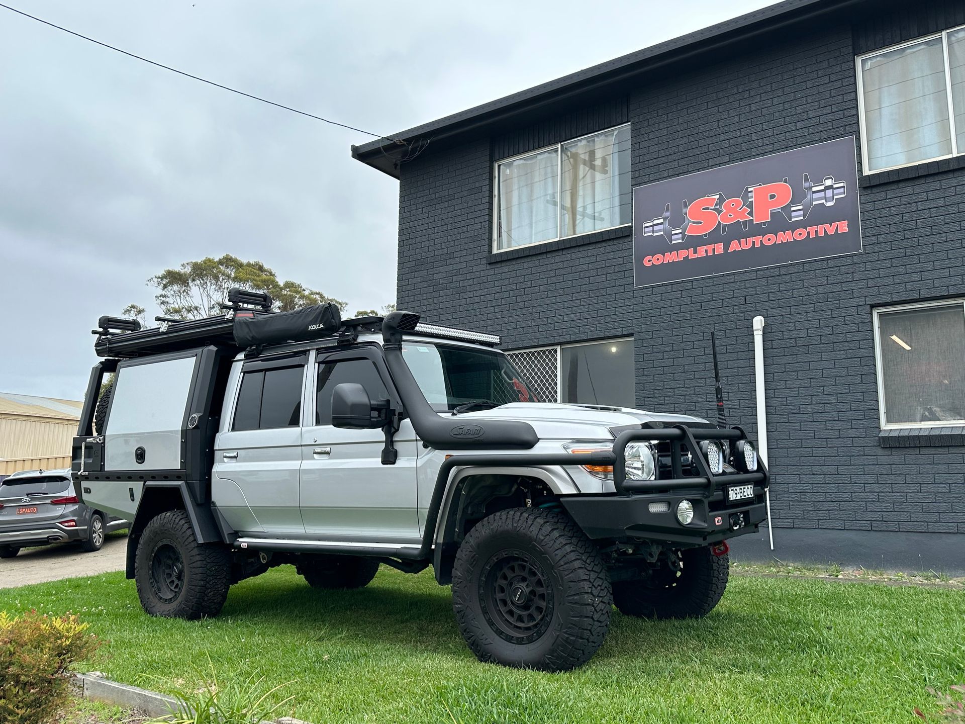 Silver off-road truck parked in front of a black building with a sign. The truck has a black bull bar and wheels — S&P Complete Automotive in Port Macquarie, NSW.