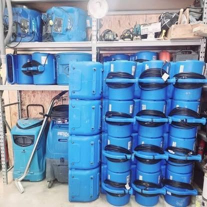 Stacked blue plastic barrels and containers stored on shelves and the floor in a workshop or warehouse