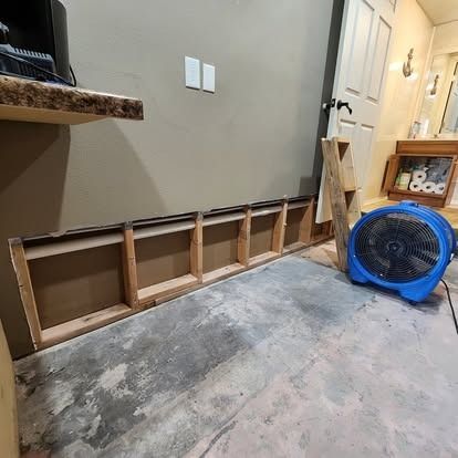 Partially built wooden wall framing along a hallway, with a blue floor fan and concrete floor setting.
