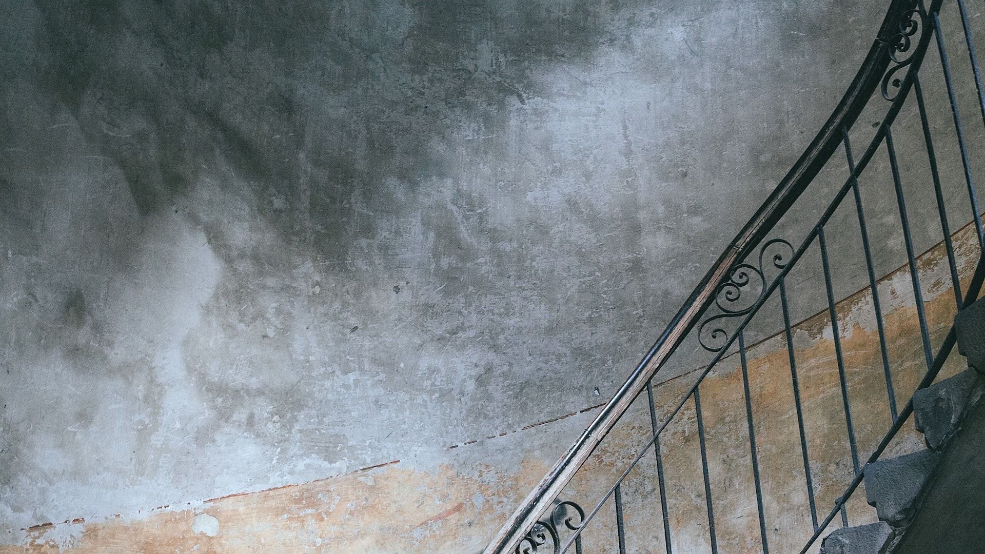 Stone staircase with black iron railing beside a weathered gray wall and floor with fire damage.