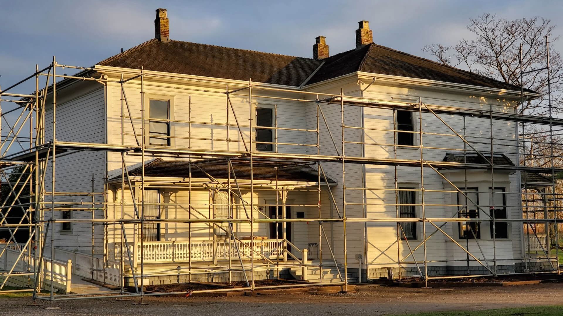 Two-story house under construction, wrapped in scaffolding at sunset.