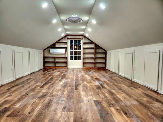 Attic room with sloped ceiling, skylights, white cabinets, and wood floor