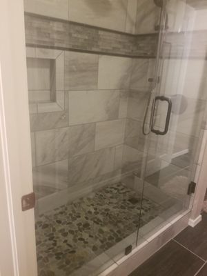 Glass shower enclosure with gray tile walls and pebble-stone floor.