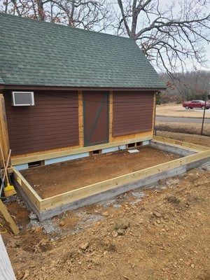 Small brown shed with green roof and unfinished wooden porch on a bare construction site