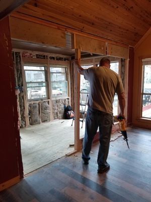 Worker standing in a wood-paneled room under renovation, holding a tool near a doorway