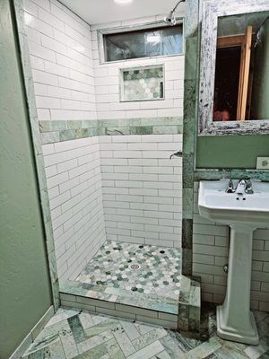 Small tiled bathroom with a shower stall, pedestal sink, and green door frame.