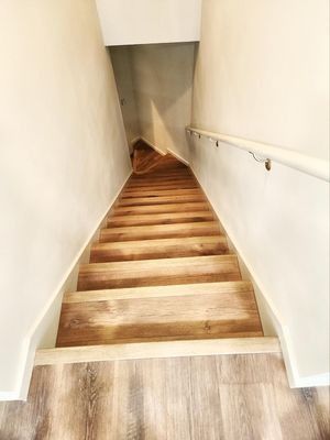 Narrow indoor stairway with wooden steps and white walls, descending steeply
