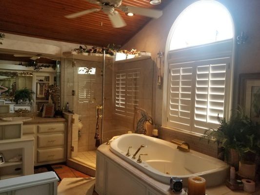Cozy bathroom with a jacuzzi tub, shuttered windows, wood ceiling, and warm lighting